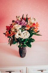 Bouquet in a vase on a chest of drawers. The bouquet consists of white roses, .lilac asters and orange alstromeries.