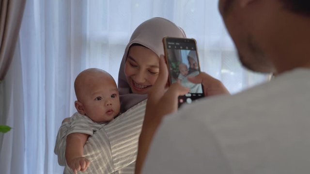 dad take picture of his wife carrying baby boy at home