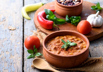 Traditional baked beans in tomato sauce cooked in retro clay pot with spices and vegetables.