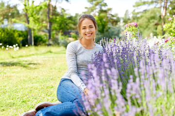 gardening and people concept - happy young woman sitting on grass near lavender flowers on summer...