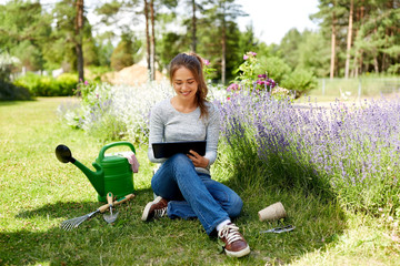 gardening, technology and people concept - happy young woman or gardener with tablet computer and garden tools in summer