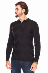 man with beard and dark hair stands on a white background in dark blue sweater with zip and collar and dark jeans, he has a gold watch on his arm and looks on the left direction © monchak