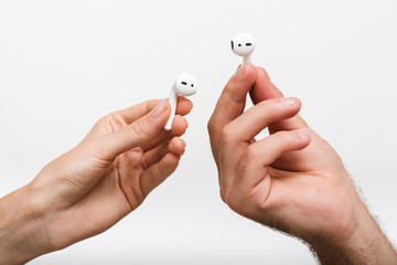 Man's and woman's hands isolated over white wall background holding earphones.