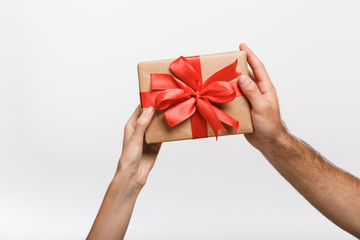 Man's and woman's hands isolated over white wall background holding present gift box.