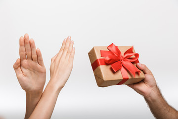Woman's hands showing stop gesture while her man isolated over white wall background holding present gift box.