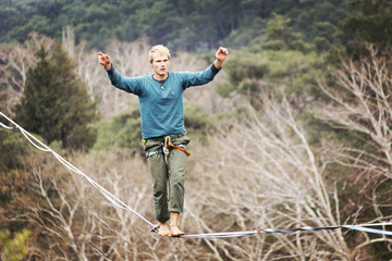 A man is walking along a stretched sling. Highline in the mountains. Man catches balance. Performance of a tightrope walker in nature. Highliner on the background of the mountains.