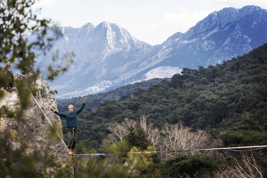 A man is walking along a stretched sling. Highline in the mountains. Man catches balance. Performance of a tightrope walker in nature. Highliner on the background of the mountains.