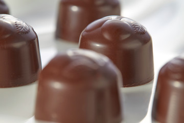 Chocolate candies with cherry filling without wrappers laid out on a white plate close-up. Selective focus.