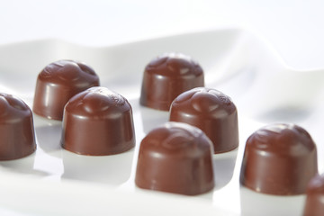 Chocolate candies with cherry filling without wrappers laid out on a white plate close-up.