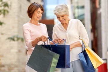 sale, consumerism and people concept - two senior women or friends with shopping bags on tallinn city street