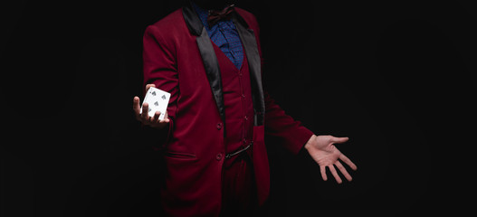 Fototapeta premium Magician young man holds playing cards in red jacket on black background