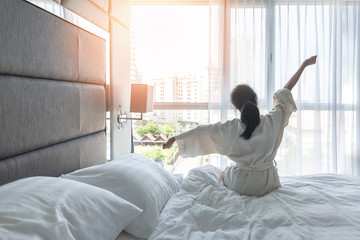 Work-life quality balance concept with lazy lifestyle of Asian girl on bed relaxing in comfort city hotel bedroom, take it easy, resting from good sleep waking up on weekend morning having a good day