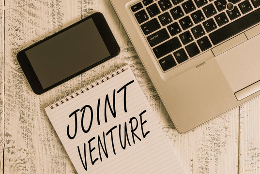 Handwriting text Joint Venture. Conceptual photo Collaboration Arrangement Parties Partnership Team Metallic laptop blank ruled notepad smartphone lying old wooden table