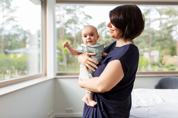 babyhood, motherhood and people concept - happy middle-aged mother holding baby daughter at home