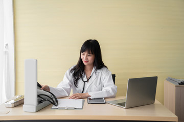 The happy female doctor sat on the working chair while working with laptop in the examination room