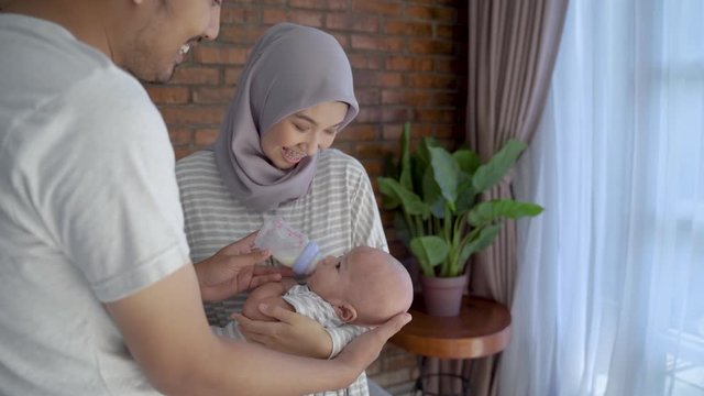 asian parent feeding baby with bottle of milk together at home