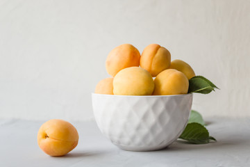 Fresh ripe apricots in a white plate on a gray background. The concept of proper and delicious food. Side view, close-up, copy space.