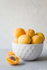 Fresh ripe apricots in a white plate on a gray background. The concept of proper and delicious food. Side view, close-up, copy space, vertical orientation