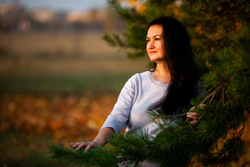 Golden autumn. Beautiful brunette caucasian woman in a blue pullover in the city park at sunset. Yellow leaves. Plus-size model.