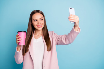 Portrait of cute cheerful lady using her cellphone making selfie holding mug with hot beverage...