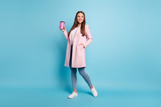 Full size photo of lovely cute cheerful girl having walk promenade holding mug wearing coat denim jeans isolated over blue background