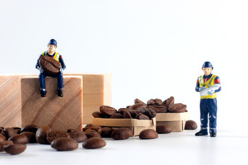 Miniature worker sitting on wooden block while carry coffee bean and below has Paper box filled with coffee beans with worker checking products
