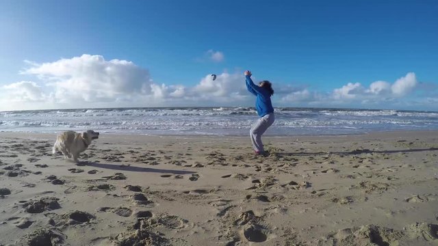 Man in blue sweater does a backflip while a dog runs by on a beach, gopro