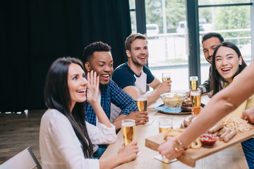 cropped view of woman holding tray with snacks near happy multicultural friends in bar