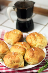 homemade fresh herb bread rolls of Provencal herbs with salt and sprig branch of rosemary. Bread rolls bakery style on white plate and red white towel cage italian style, black geyser coffee machine