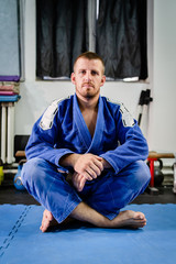 Young bjj brazilian jiu jitsu or judo athlete jujitsu fighter sittin on the tatami mats floor on the training wearing blue kimono gi