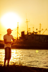 Fototapeta premium Young man fishing at sea from the shore at sunset. soft light. fisherman uses spinning