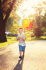 Cute adorable little Caucasian boy toddler child with colorful balloons in park outdoor. Kid enjoying playing. Happy birthday holiday celebration. Candid authentic lifestyle childhood moment.