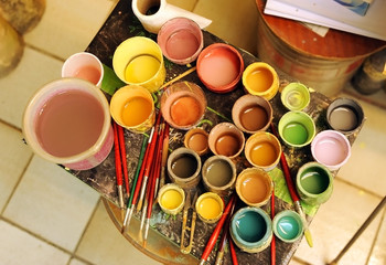 Many brushes and glass jars with ceramic colored pigments prepared to paint tiles by hand in the potter's workshop