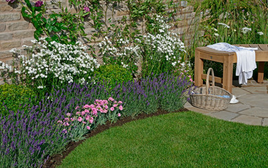 Close up of a flower border in a corner of a walled cottage garden with basket and coffee break