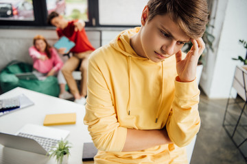 pensive boy in yellow hoodie and laughing classmates bullying him
