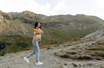 Naklejka na ściany i meble stylish traveler girl in hat with backpack jumping in mountains. happy hipster woman having fun on top of mountain. space for text. wanderlust and travel concept. atmospheric moment