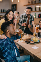 selective focus of handsome african american man drinking light beer while spending time in pub together with cheerful multicultural friends