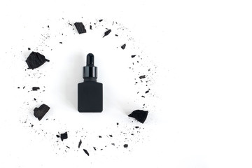 Black serum bottle surrounded by charcoal on white background with copy space, Mockup product