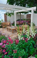 Obraz premium A contemporary garden with terraced area and stylish wooden furniture surrounded by colourful flowering borders