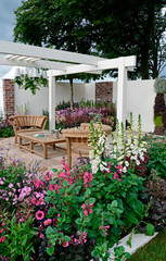 A contemporary garden with terraced area and stylish wooden furniture surrounded by colourful...