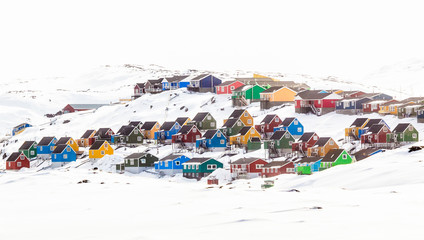 Fototapeta na wymiar Multiple colorful Inuit houses and cottages on the hill covered in snow, Aasiaat city, Greenland