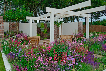 Fototapeta na wymiar A contemporary garden with terraced area and stylish wooden furniture surrounded by colourful flowering borders