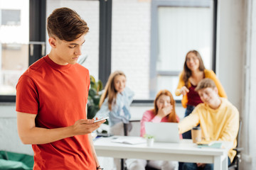 group of schoolchildren with laptop laughing at sad boy holding smartphone