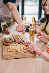 cropped view of multicultural friends sitting at pub near tray with fried onion rings, sausages and french fries