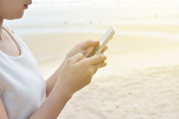 Happy girl watching streaming videos in smart phone on the beach with the ocean and a warm light.