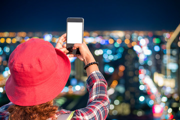 Young female tourists using mobile phones to take pictures bokeh background of Bangkok City skyline with urban skyscrapers at night time. Bangkok is known as a paradise city that never sleeps.