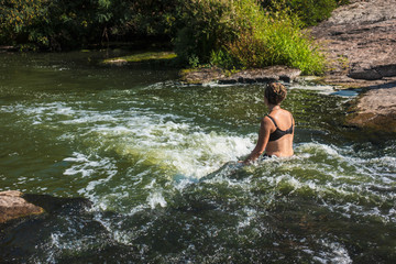 A woman sits on a stone in a stream of fast water.