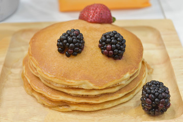 Fresh pancakes many color stacked layered with orange on wooden plate.