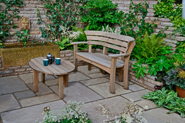 Close up of a wooden garden seat and table in a terrace in a walled garden with seletion of plants