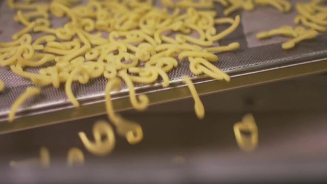 Slow motion of short raw pasta passing and jumping on a conveyor belt in a pasta factory. 